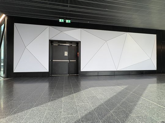 Dieselbe Wand unbeleuchtet, frontal: weiße Pyramidenflächen, in der Mitte die eingelassene Tür